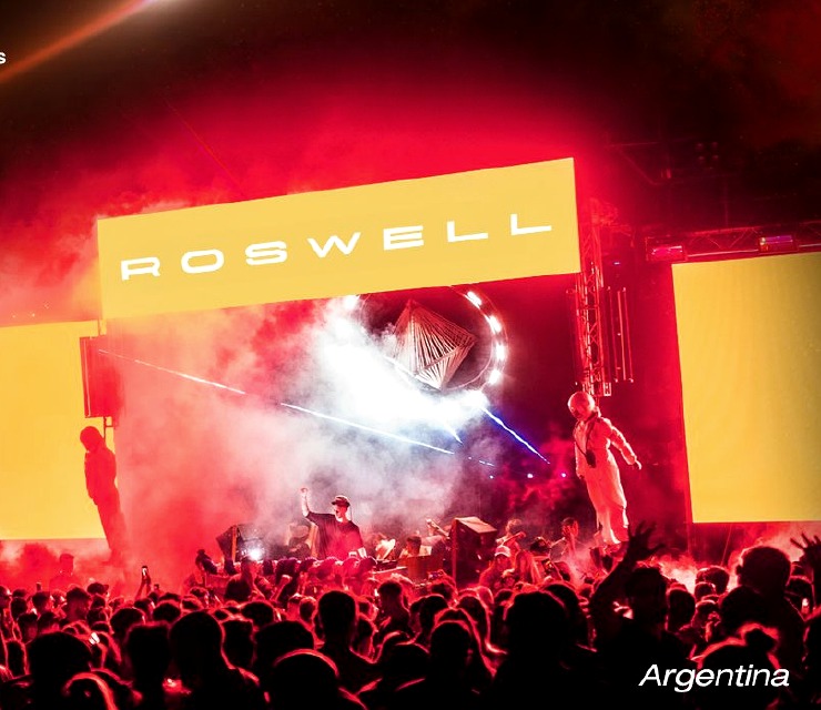 Escenario Roswell iluminado en rojo frente a una multitud.